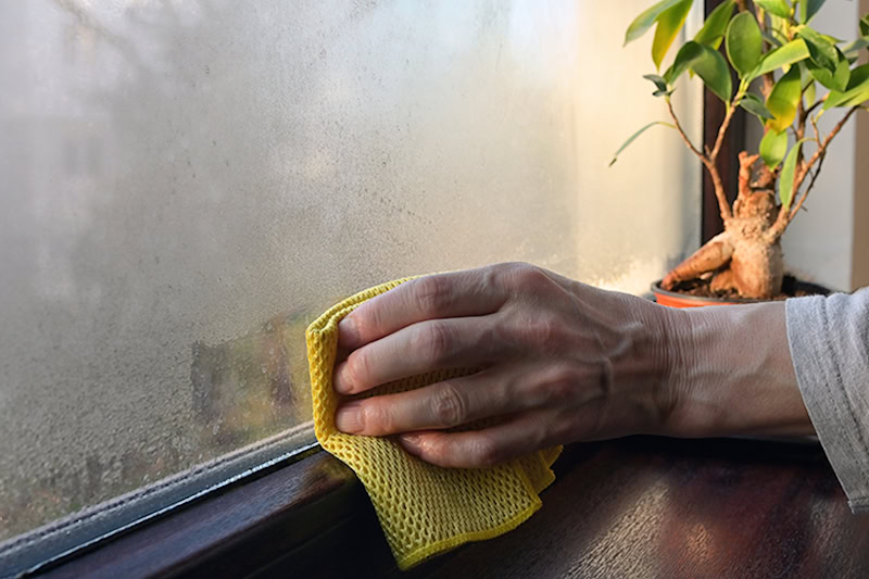 hand wiping away condensation from window at home.